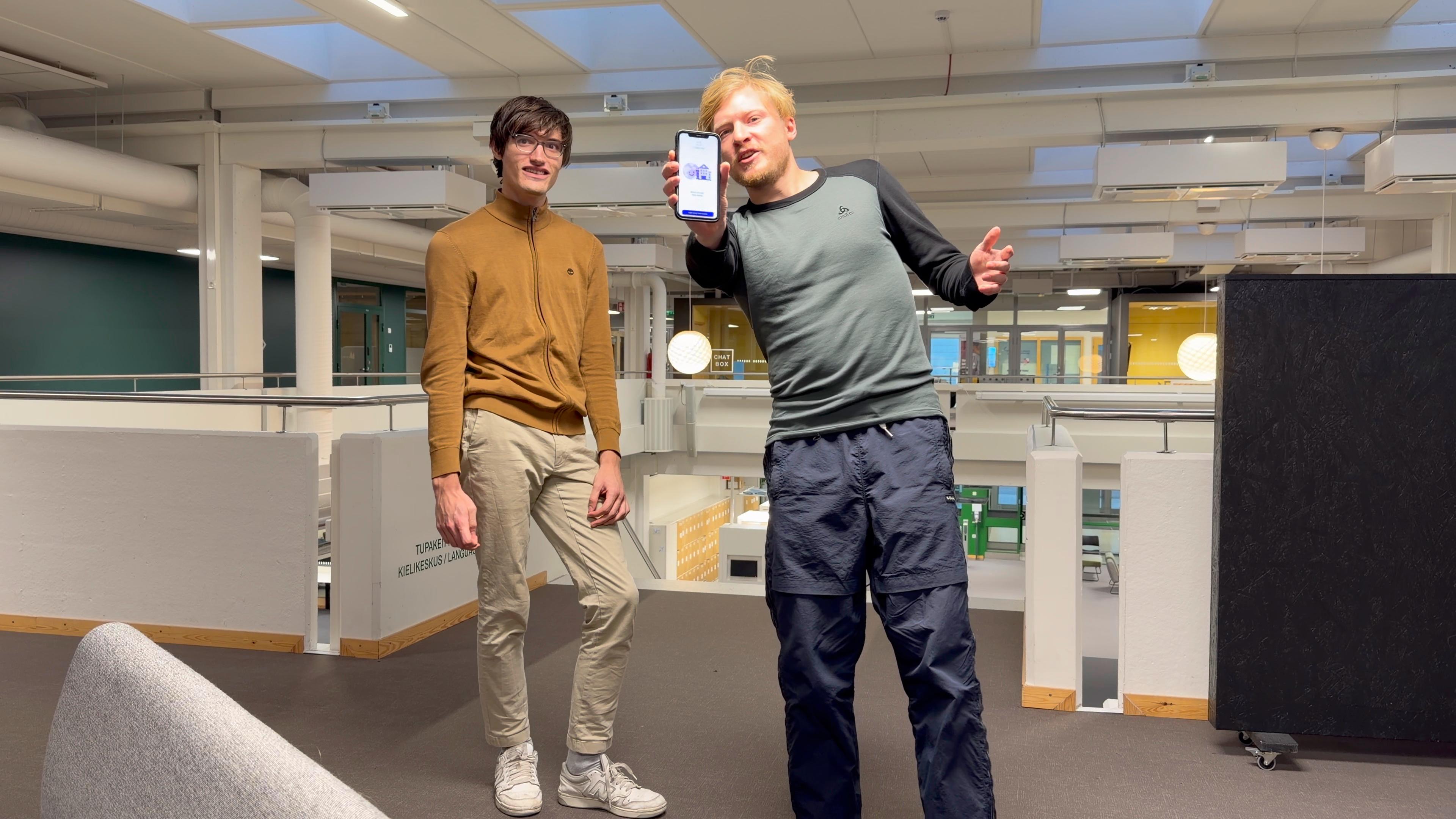 Two team members presenting the UniBorrow app on a phone in the university common space